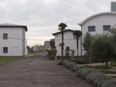 Veniamo introdotti in un cortile nel quale si stagliano numerose strutture bianche ciascune con due ordini di finestre. Tutt'intorno un verdissimo prato, ghiaia e cespugli, alberi d�ulivo e alte palme con accanto alti vasi di terracotta